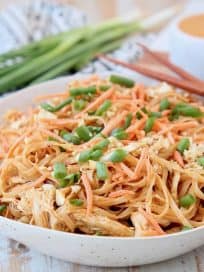Pressure cooker chicken noodles with thai peanut sauce in bowl with diced green onions, shredded carrots and peanuts