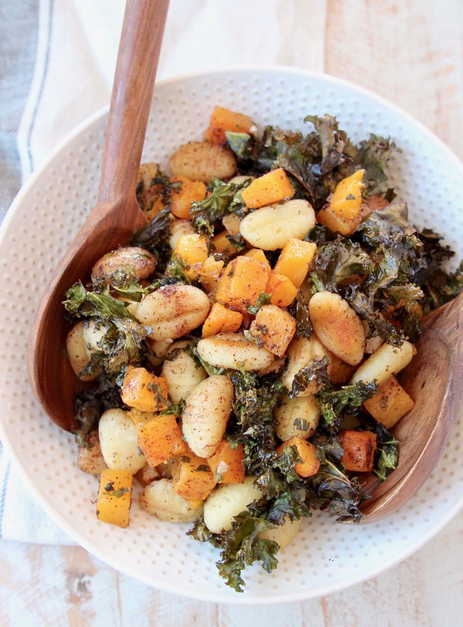 Gnocchi, butternut squash and kale in large white bowl with wooden serving spoons