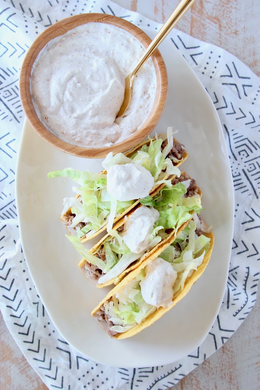 Ground beef tacos in crispy shell with shredded lettuce and french onion dip on plate with bowl of french onion dip with gold spoon