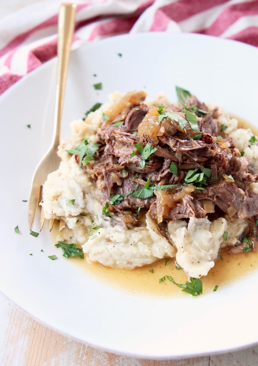 French onion pot roast on top of mashed potatoes with fresh parsley on a while plate with gold fork