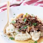 French onion pot roast on top of mashed potatoes on white plate with gold fork
