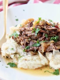 French onion pot roast on mashed potatoes with fresh parsley on white plate with gold fork