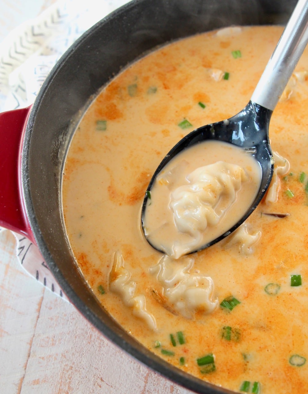Thai coconut soup with potstickers in large red cast iron pot with spoon coming out of soup holding a potsticker