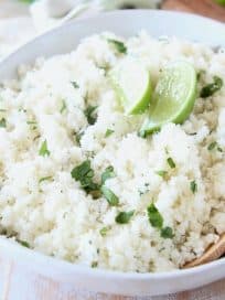 Cilantro lime rice in large white bowl with wooden spoon and lime wedges on top