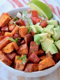 Diced roasted sweet potatoes in quinoa bowl with diced avocado, pico de gallo and lime wedge with copper fork
