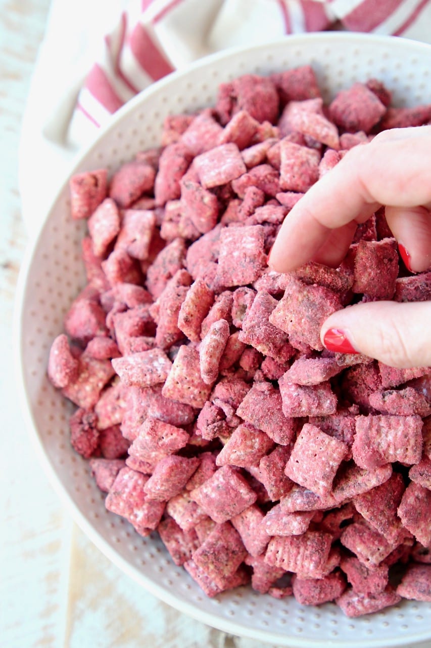 Hand reaching in grabbing red velvet puppy chow out of a white bowl