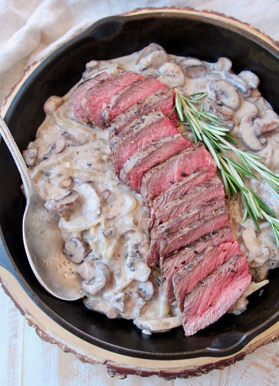 Overhead shot of sliced wagyu steak in cast iron skillet with creamy mushrooms and rosemary sprigs