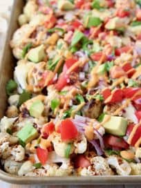 Cauliflower nachos on gold sheet pan topped with diced tomatoes and avocado