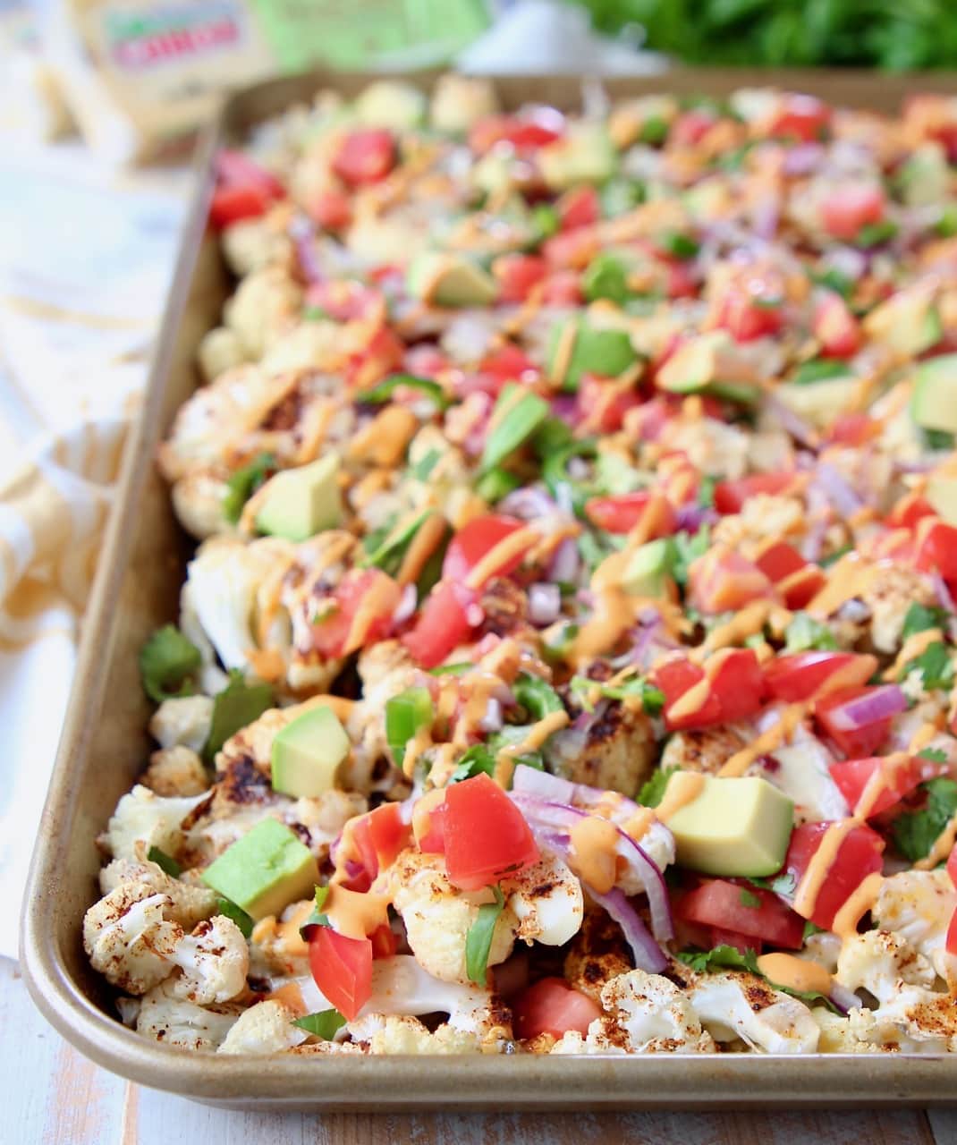 Cauliflower nachos on baking sheet topped with diced tomatoes and avocado