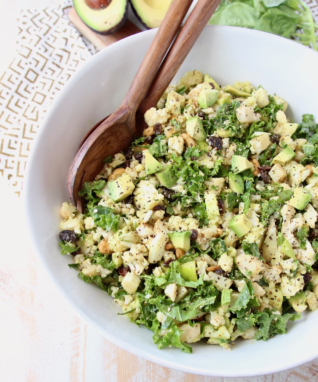 Overhead shot of cauliflower salad with chopped kale and avocado in large white bowl