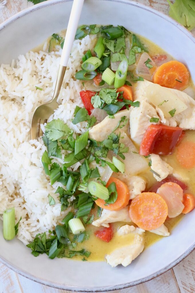 vegetables and chicken in yellow curry sauce in bowl with cooked white rice