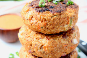 Buffalo chicken burger patties stacked up on plate with diced green onions