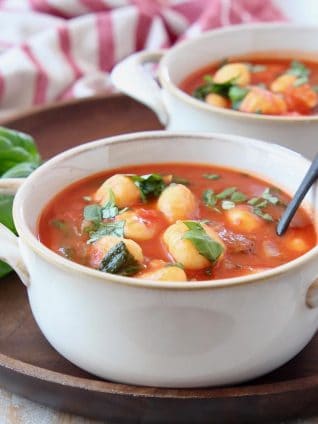 Tomato basil gnocchi soup in white bowls on wood tray