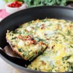 Slice of vegetable frittata being lifted out of skillet with silver spatula