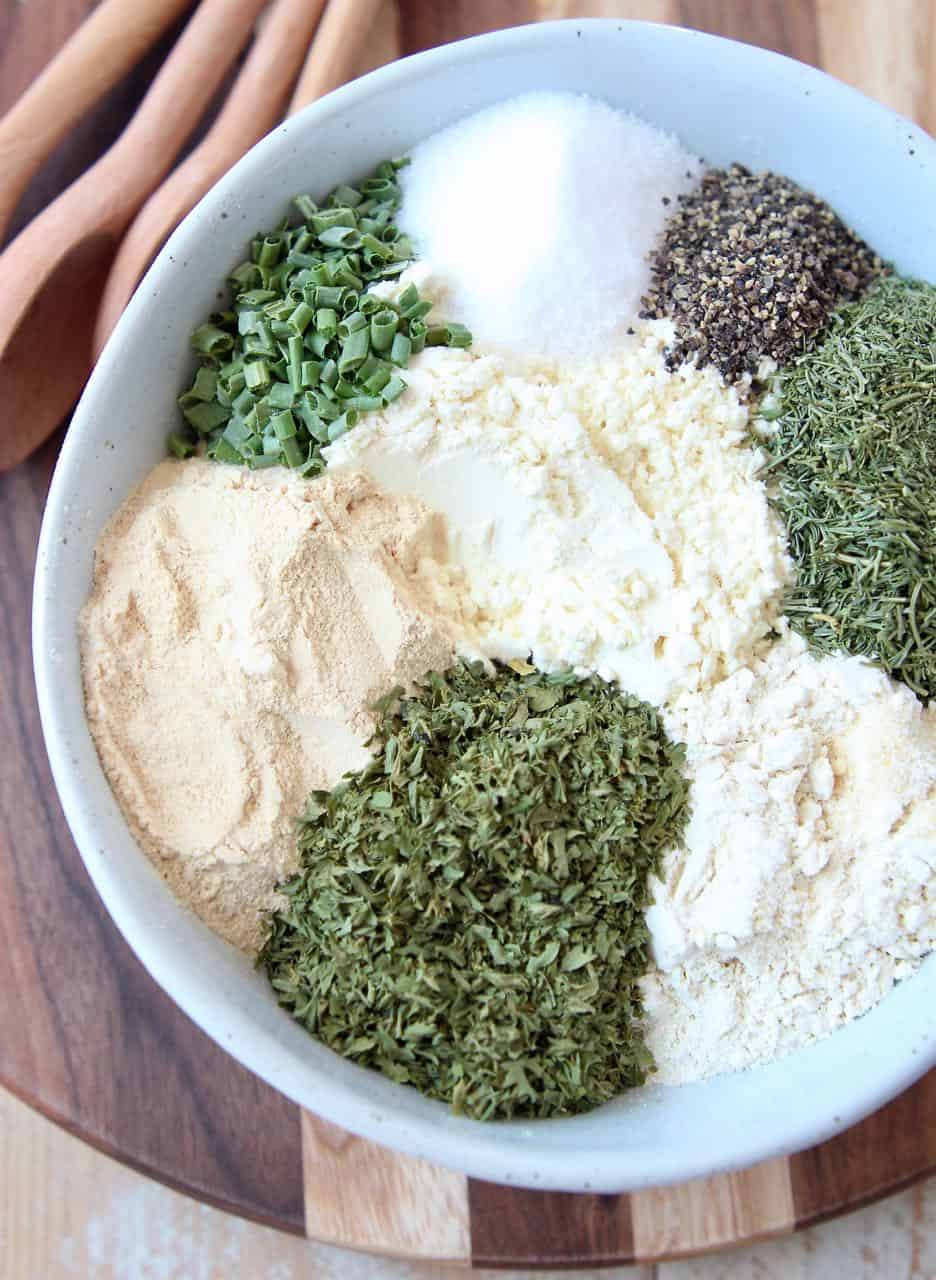 Ranch seasoning mix ingredients separated in white bowl on wood cutting board