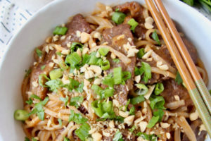 Sliced beef, noodles and green onions in bowl, with small bowl of peanut sauce on the side