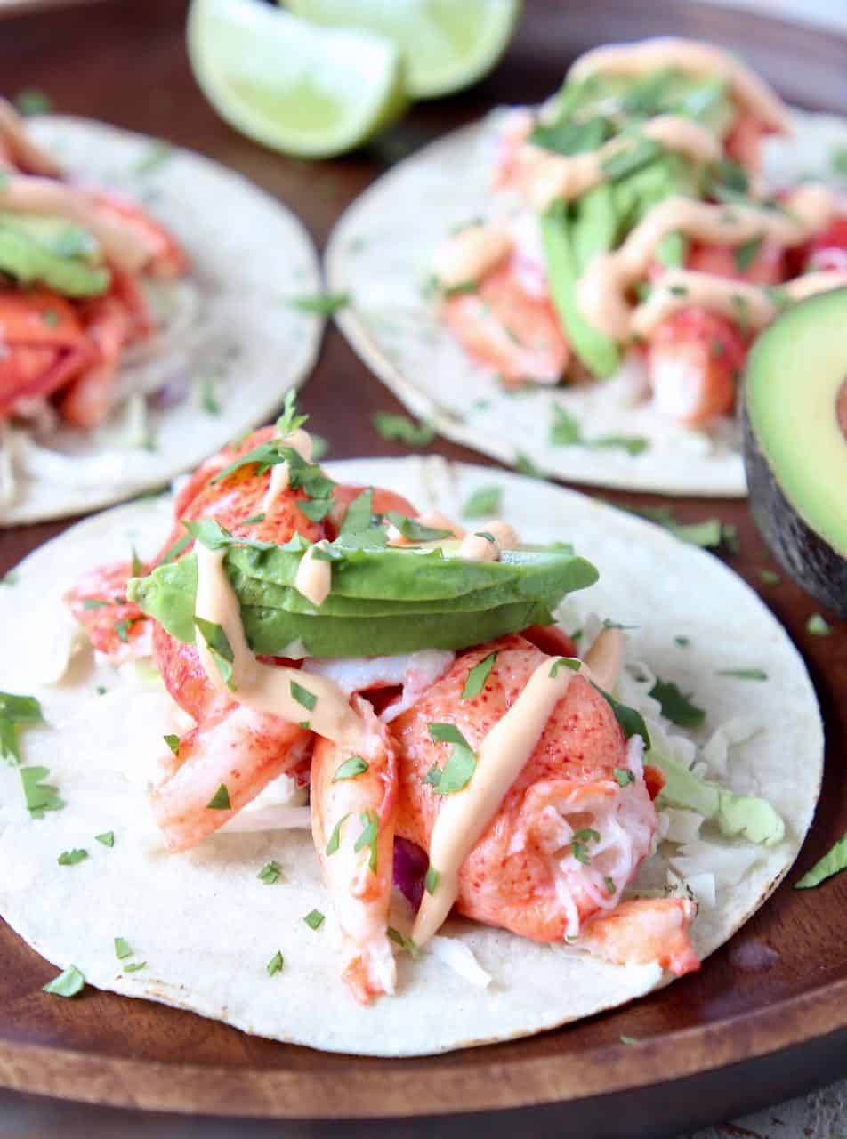 Lobster tacos topped with avocado on wood serving tray
