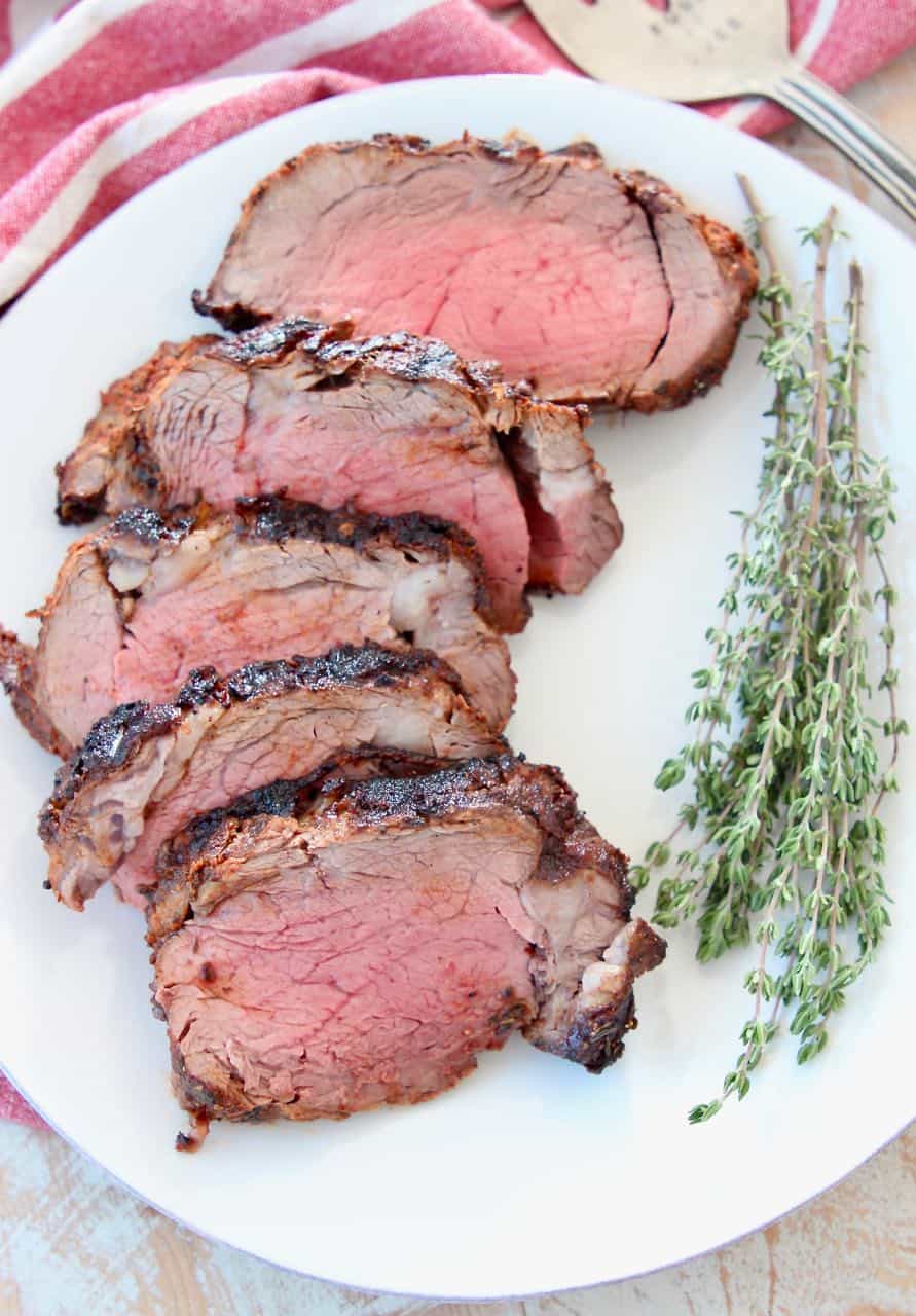 Slices of blackened beef tenderloin on white plate with fresh herbs