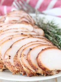 Sliced smoked turkey breast on plate with fresh rosemary and thyme