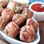 Bacon wrapped meatballs in white dish with bbq sauce on the side