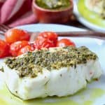 Sea bass covered in pesto on plate with cherry tomatoes