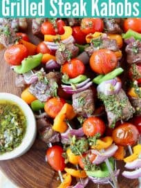 Steak and veggie skewers stacked up on wood serving tray