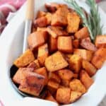 roasted cubed sweet potatoes in bowl with serving spoon and rosemary sprigs