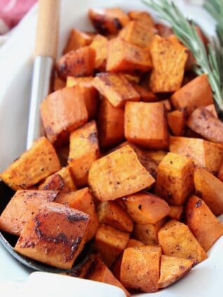roasted cubed sweet potatoes in bowl with serving spoon and rosemary sprigs