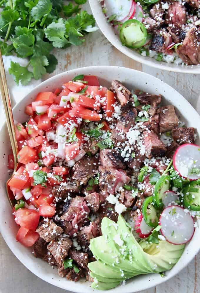 grilled steak in bowl with diced tomatoes and sliced avocado