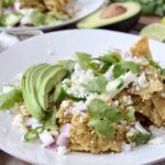 chilaquiles verdes on white plate topped with fresh cilantro and sliced avocado