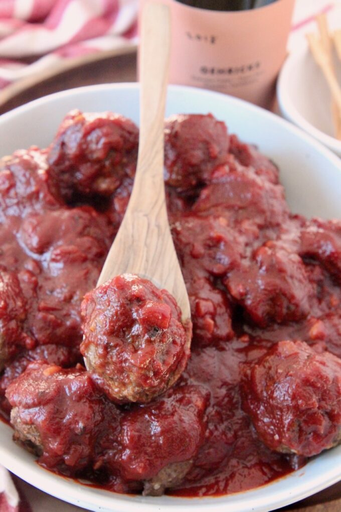 meatball covered in bbq sauce on spoon in bowl of meatballs