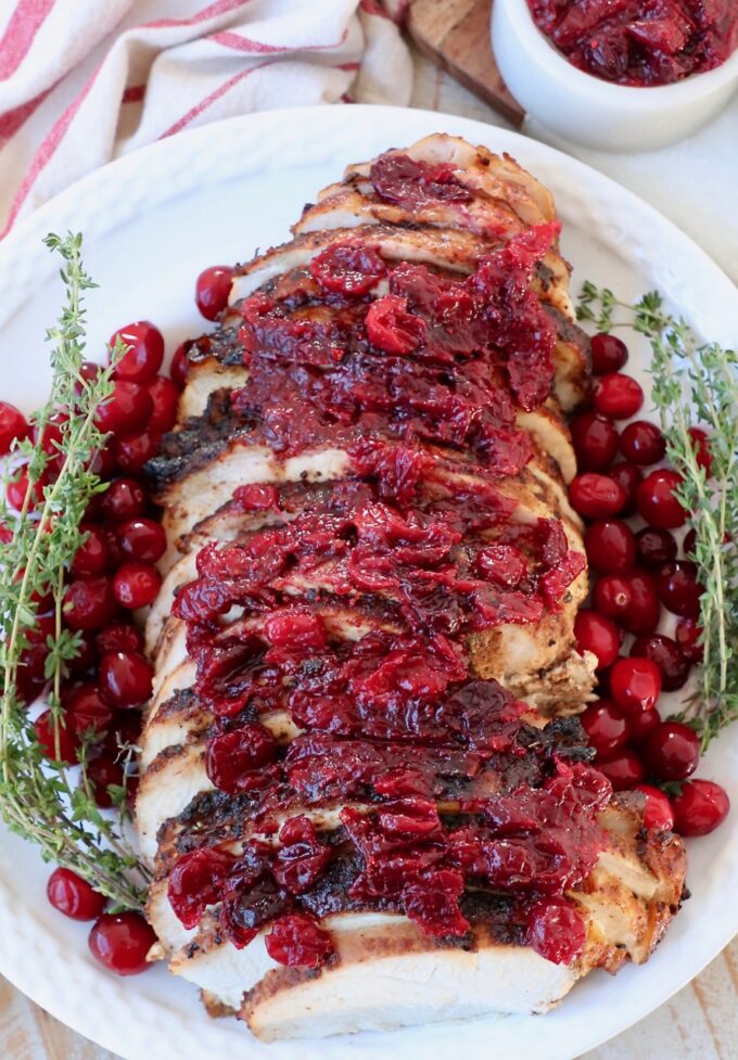 sliced turkey breast on plate with fresh cranberries and thyme