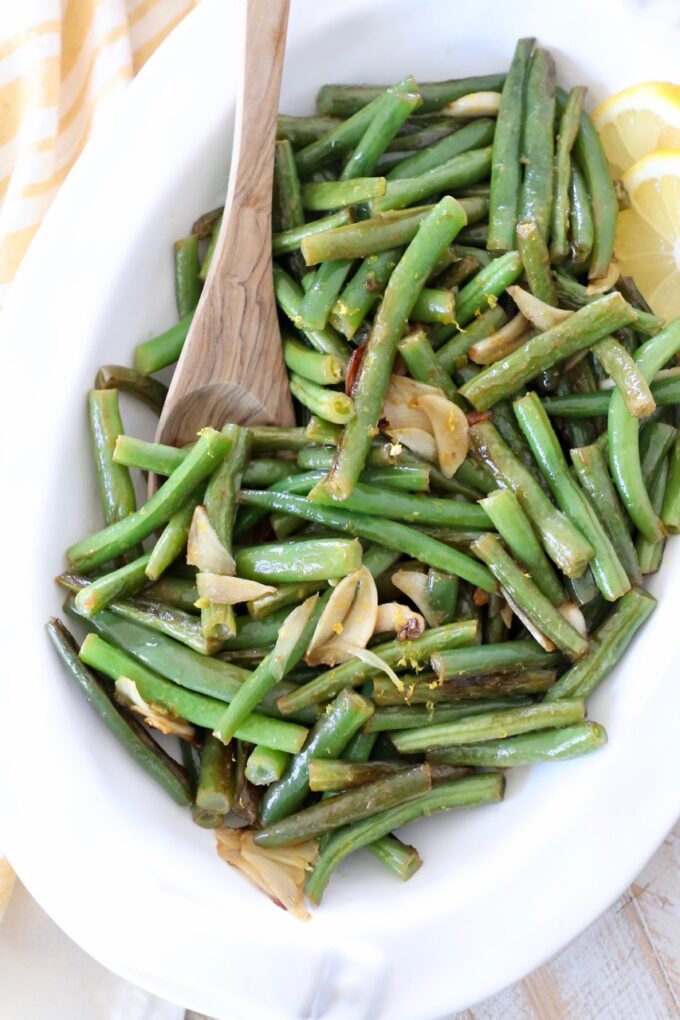 garlic green beans in white serving dish with wooden serving spoon