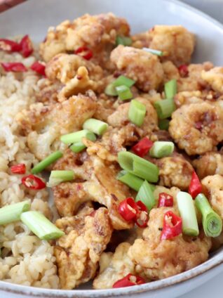 general tso's cauliflower in bowl with diced green onions, red peppers and brown rice