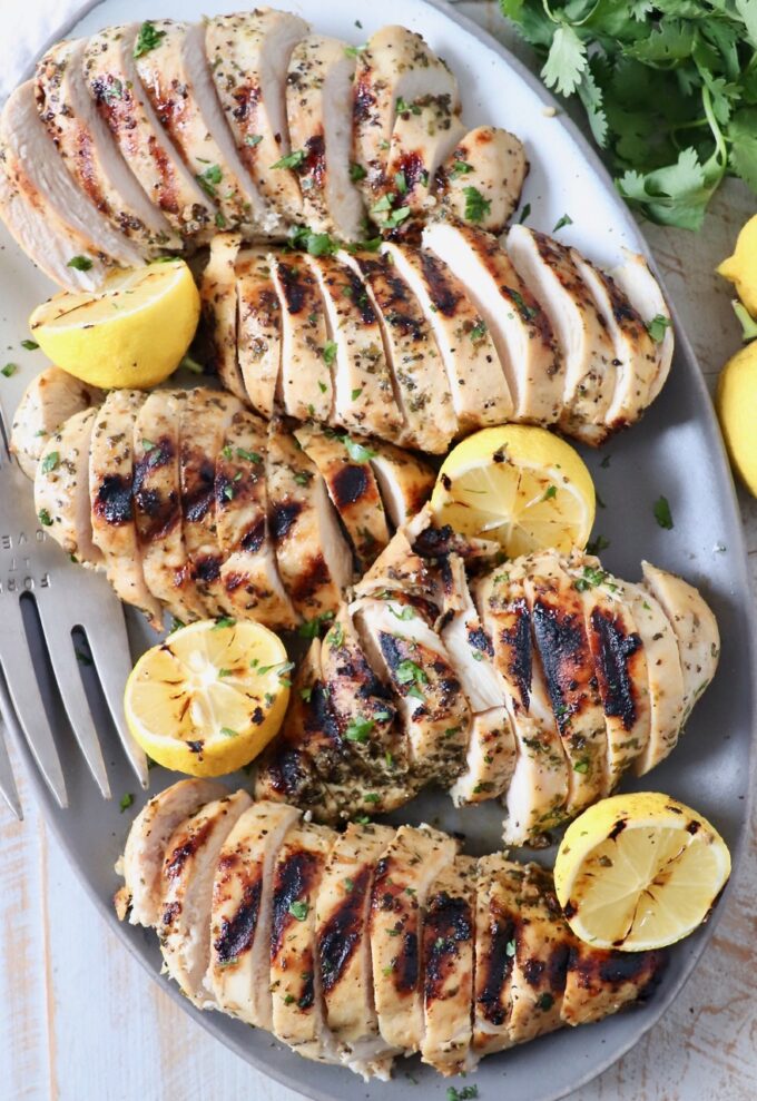 sliced grilled chicken breasts on plate with lemons