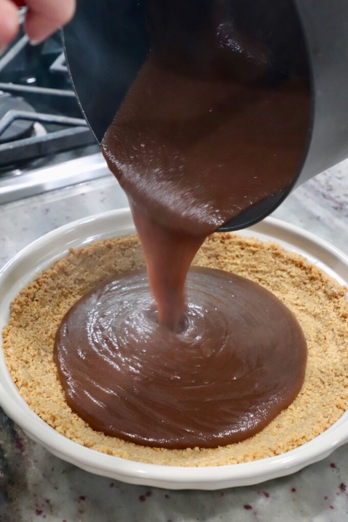 chocolate filling pouring from saucepan into graham cracker pie crust