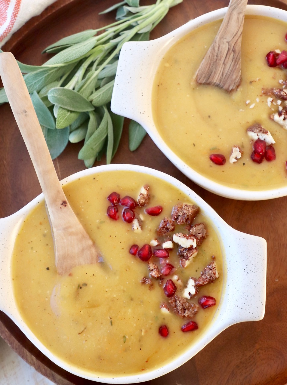 acorn squash soup in two bowls with spoons topped with walnuts and pomegranate seeds