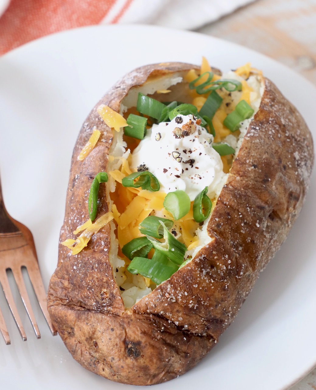 baked potato on plate filled with diced green onions, cheese and sour cream