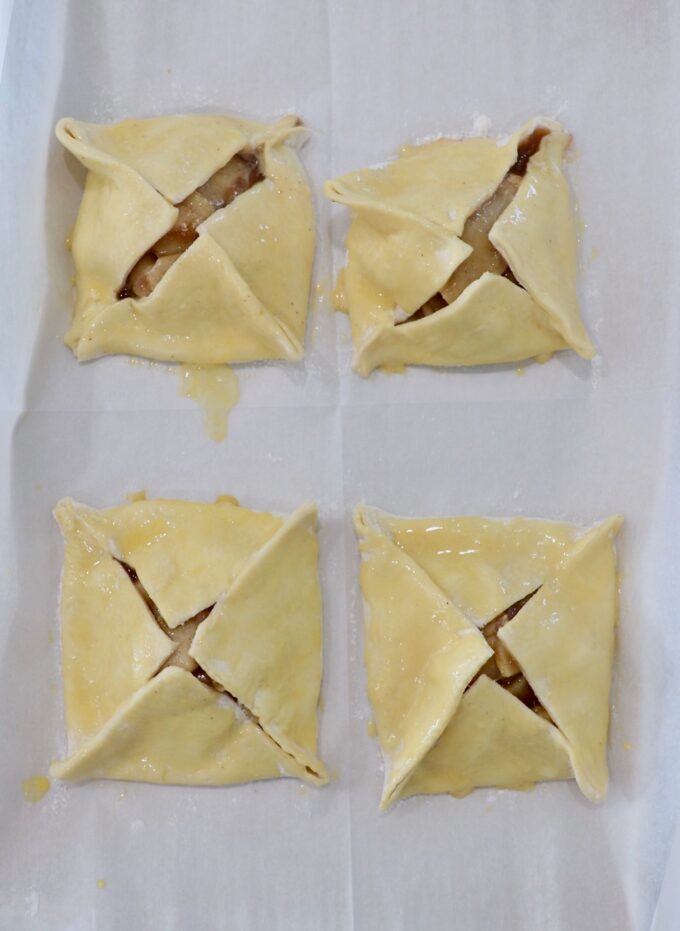 four uncooked apple danish brushed with egg wash on parchment paper