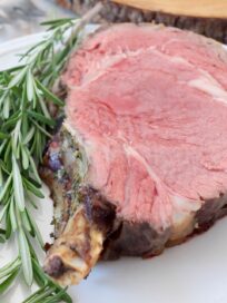 slice of bone-in prime rib on white plate with fresh rosemary sprigs