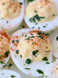 prepared deviled eggs topped with parsley and paprika on white plate