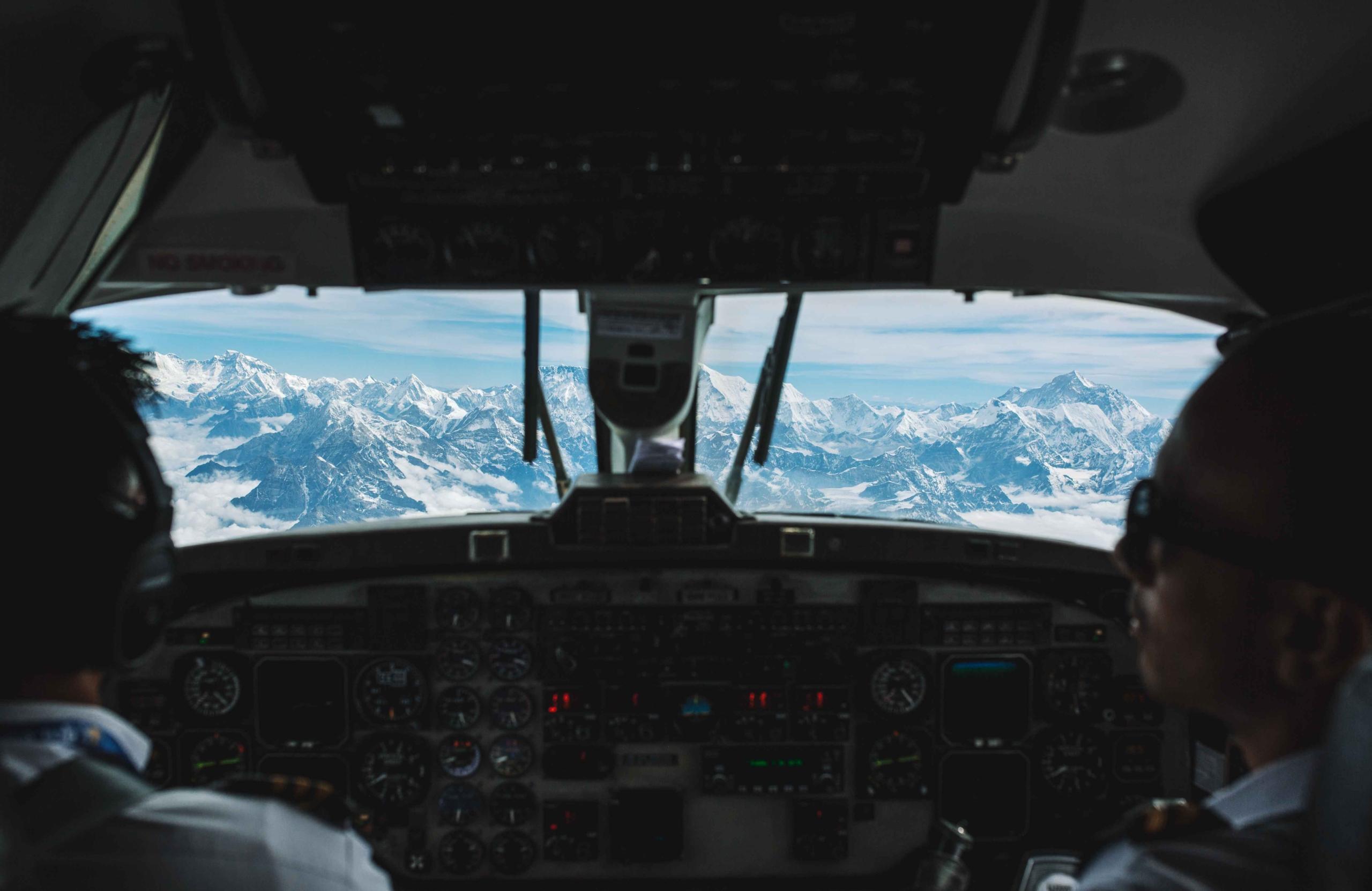 Pilots in a cockpit on a Mount Everest flight experience; mountains and clouds seen from the window.