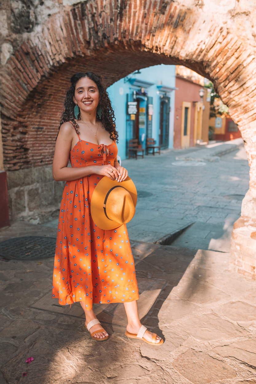 A woman in an orange dress holding a yellow hat on a Oaxaca tour photoshoot.