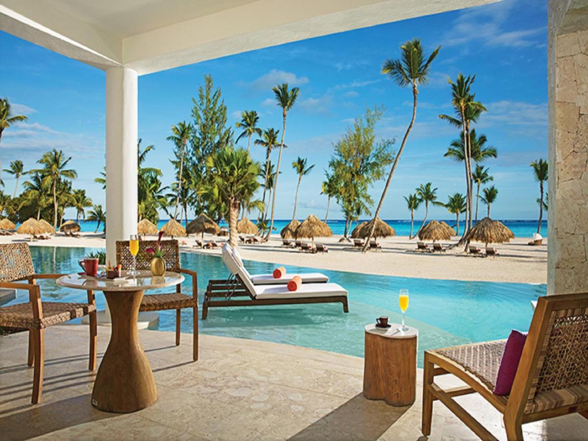 Outdoor dining area, swimming pool, huts, palm trees, and beach at a resort in Cap Cana, Dominican Republic.
