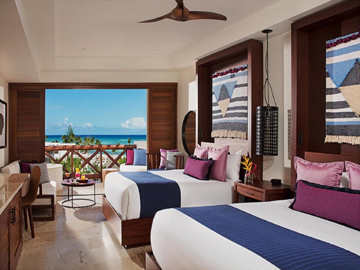 A bedroom with two beds, other furniture, and a view of the sea in a Cap Cana resort.