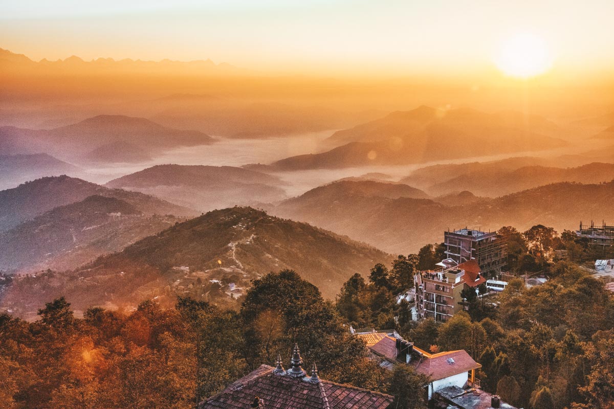 A residential area in Nagarkot surrounded by mountains at sunrise.
