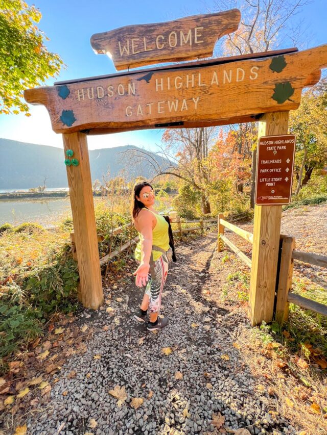A woman hiking, photographed under a welcome arc at the Cornish Estate Trail