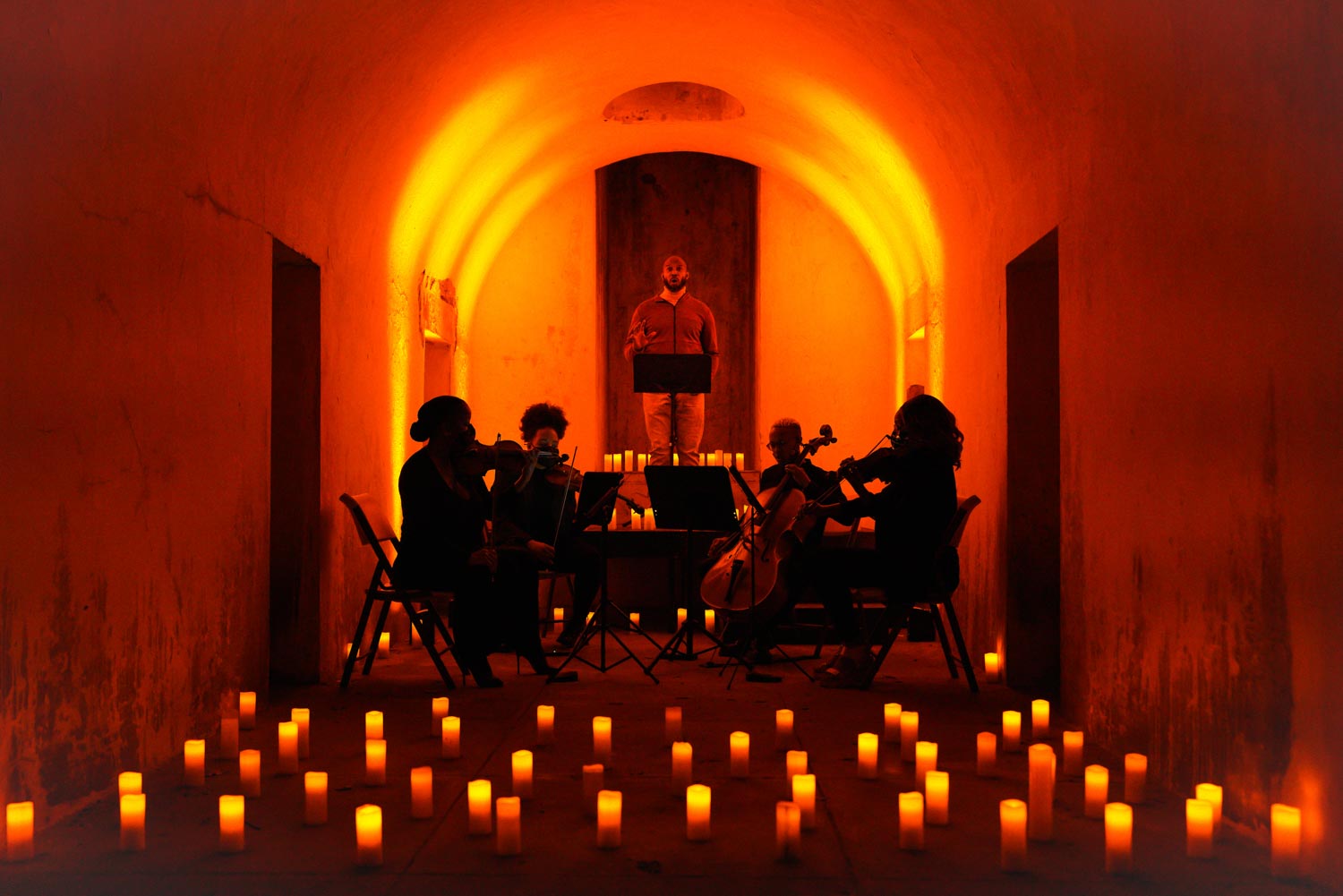 A string quartet and a vocalist performing in a dark room in the catacombs of Green-Wood Cemetery, surrounded by candles