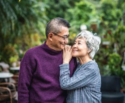 Close-up of smiling senior Chinese woman standing face to face with her contented bespectacled husband.