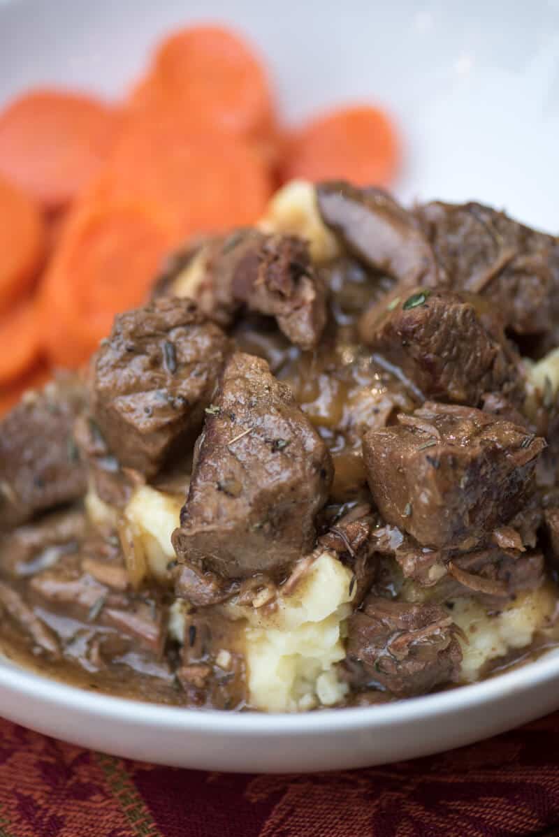  A close up image of the beef tips over a mound of mashed potatoes in a white serving bowl.